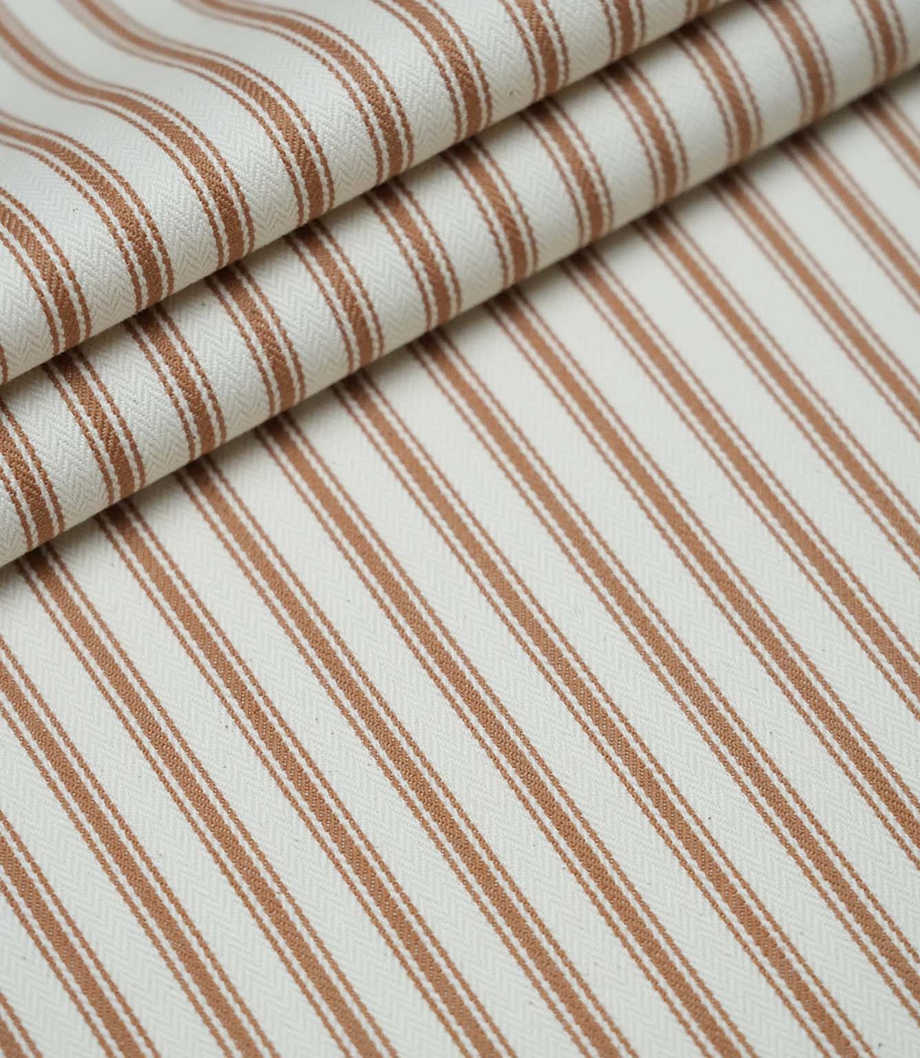 Layered folds of burnt orange ticking stripe fabric displaying the fine herringbone weave and classic striped design.