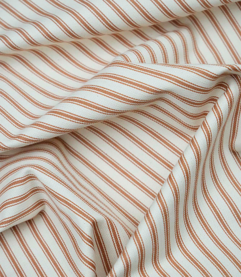 Burnt orange ticking stripe fabric draped to show its soft handle, classic stripe pattern and woven herringbone texture.