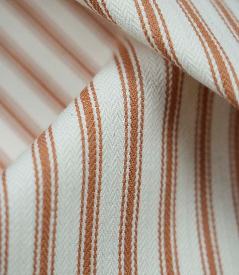 Close-up detail of burnt orange ticking stripe fabric showing the fine woven texture and warm burnt orange stripe pattern.