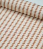 Rolled burnt orange ticking stripe fabric highlighting the warm striped design and subtle woven herringbone texture.