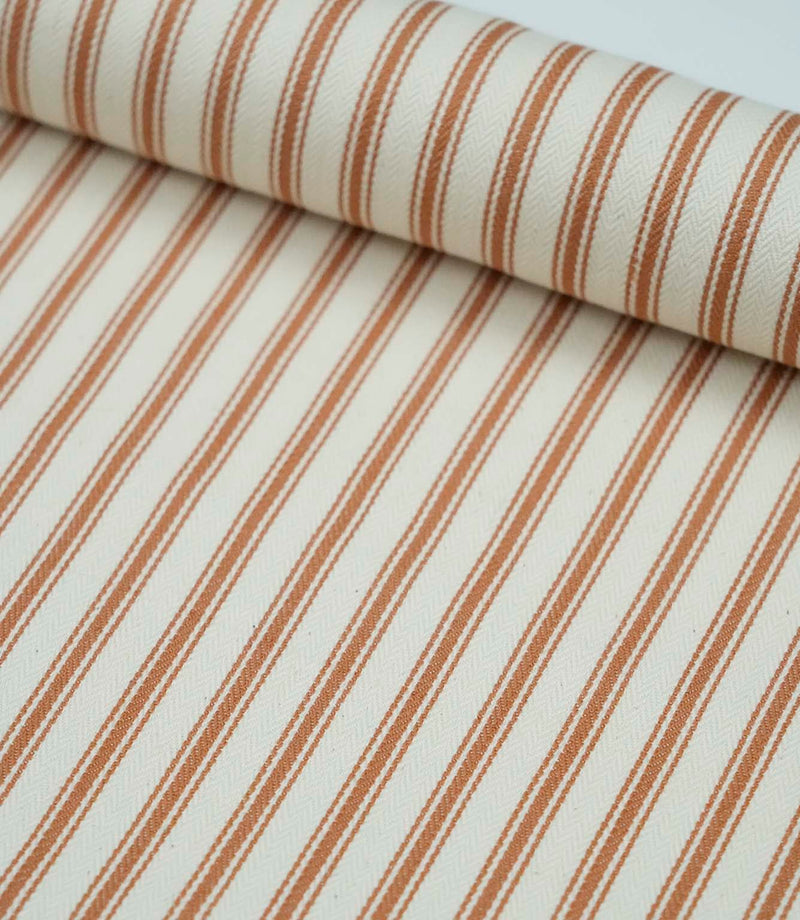 Rolled burnt orange ticking stripe fabric highlighting the warm striped design and subtle woven herringbone texture.