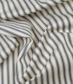 Grey ticking stripe fabric draped to show its soft handle, classic stripe pattern and woven herringbone texture.