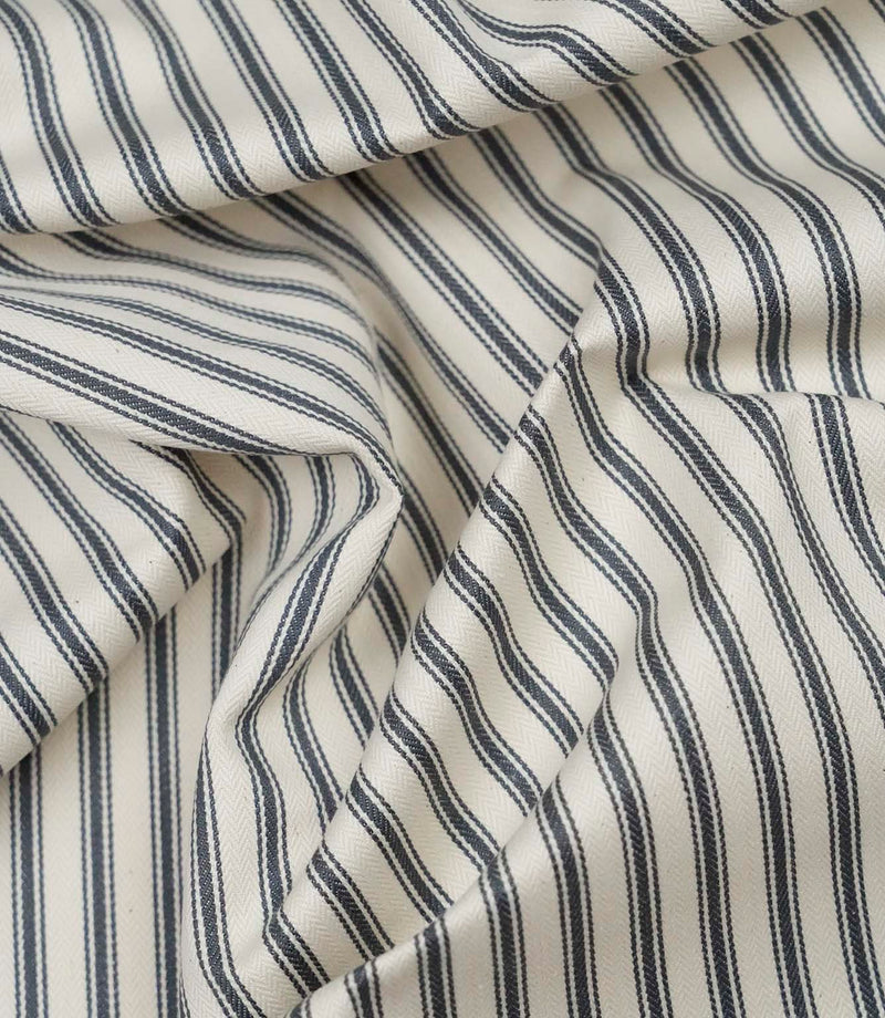 Grey ticking stripe fabric draped to show its soft handle, classic stripe pattern and woven herringbone texture.