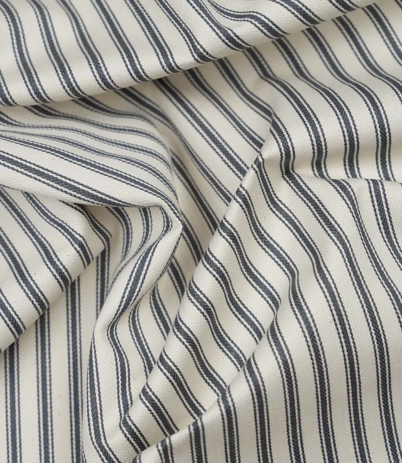 Grey ticking stripe fabric draped to show its soft handle, classic stripe pattern and woven herringbone texture.