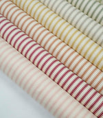 Collection of ticking stripe fabrics in blush pink, red, burnt orange, mustard, grey and sage green colourways with woven herringbone texture.