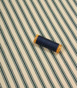 Indigo ticking stripe fabric displayed flat with a coordinating navy thread spool, showcasing the traditional striped design and woven texture.