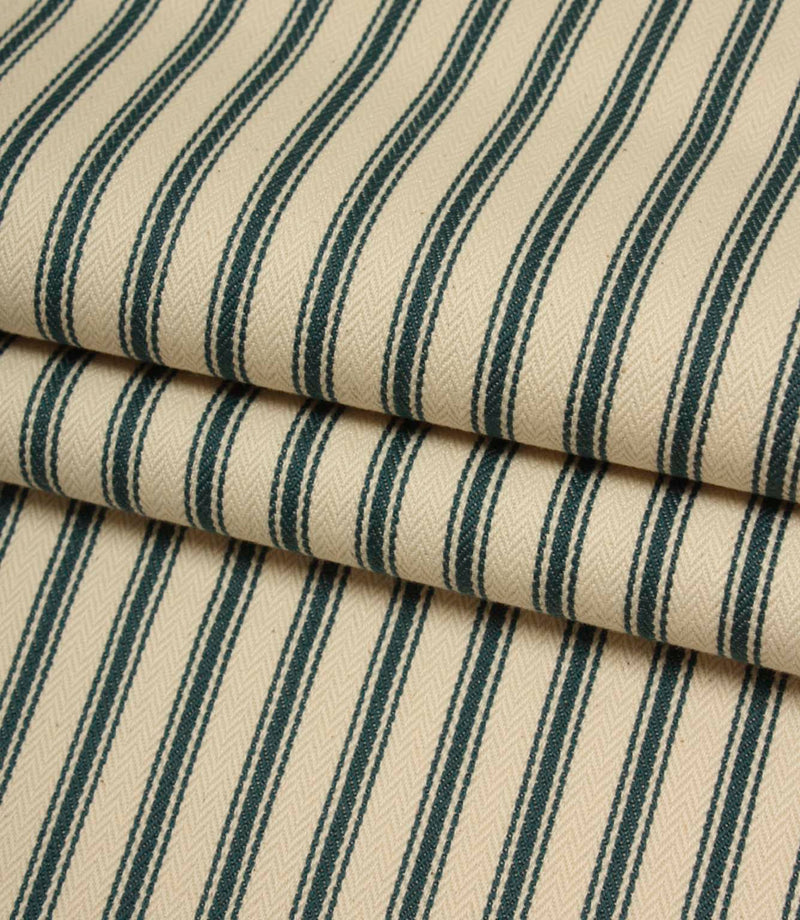 Folded indigo striped fabric revealing the soft drape, classic ticking pattern, and textured herringbone weave on an ivory background.