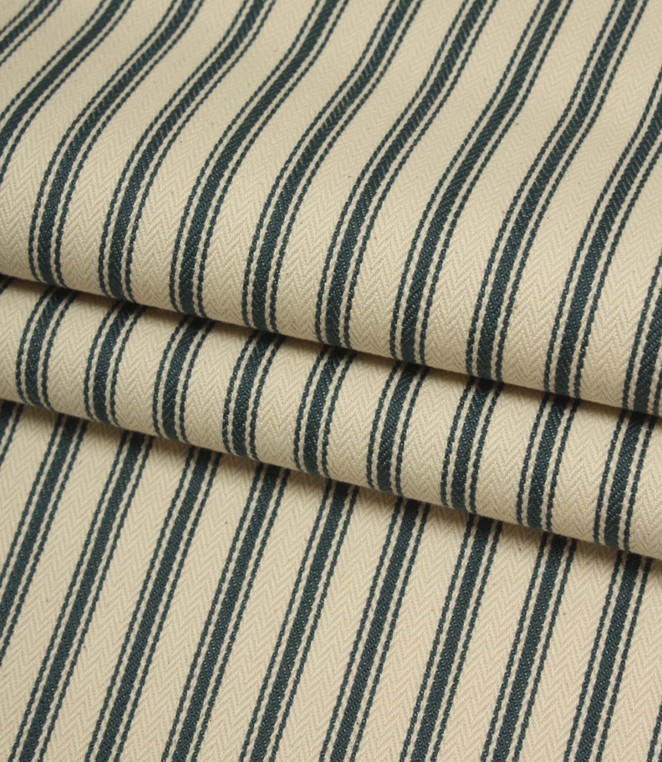 Folded indigo striped fabric revealing the soft drape, classic ticking pattern, and textured herringbone weave on an ivory background.