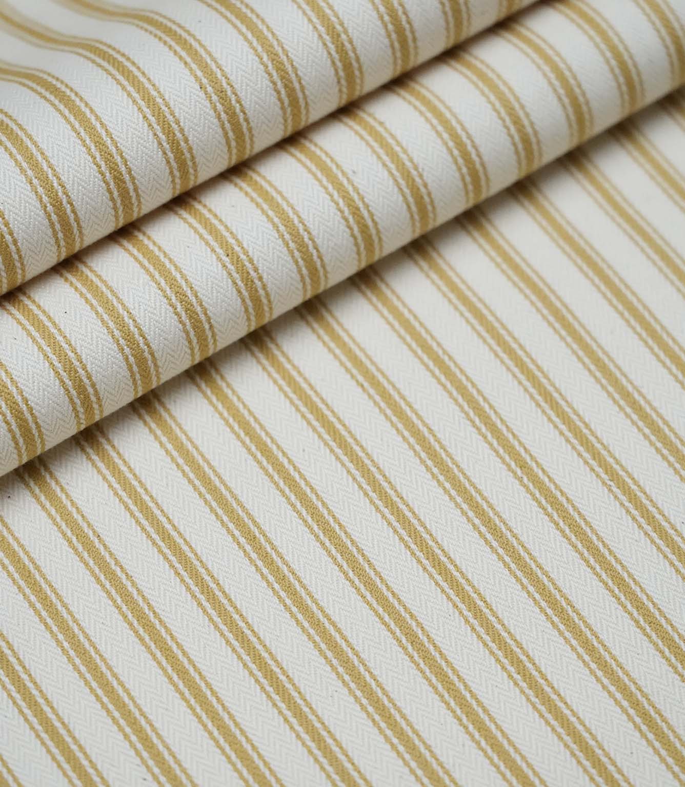 Layered folds of ochre ticking stripe fabric displaying the fine herringbone weave and classic striped design.