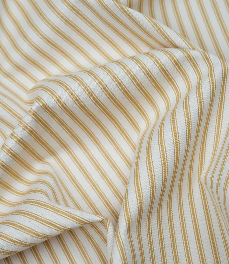Ochre ticking stripe fabric draped to show its soft handle, elegant stripe pattern and woven herringbone texture.