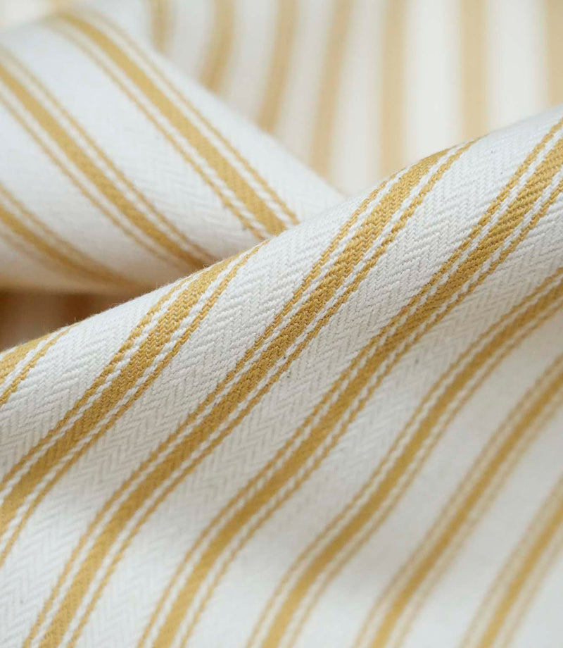 Close-up detail of ochre ticking stripe fabric showing the fine woven texture and warm ochre stripe pattern.