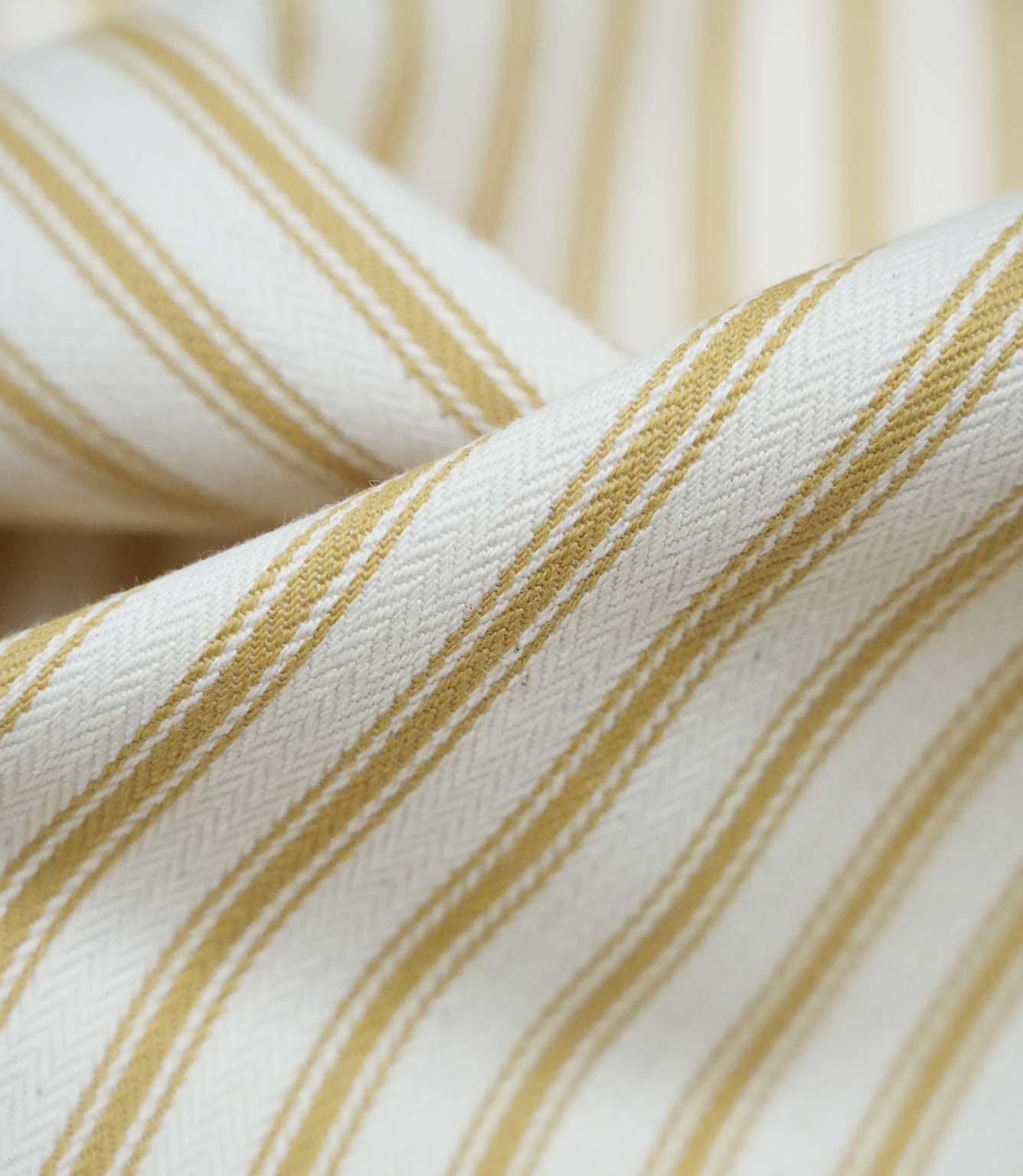 Close-up detail of ochre ticking stripe fabric showing the fine woven texture and warm ochre stripe pattern.