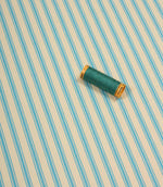 Pacific blue ticking stripe fabric shown on the diagonal with matching blue thread spool for colour reference.