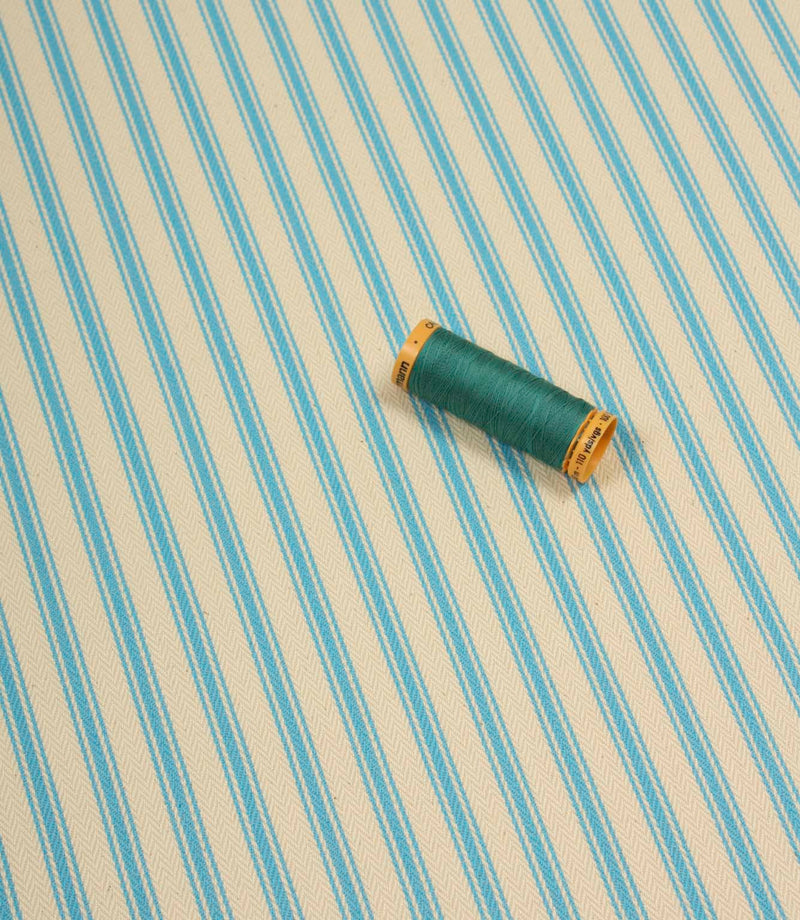 Pacific blue ticking stripe fabric shown on the diagonal with matching blue thread spool for colour reference.