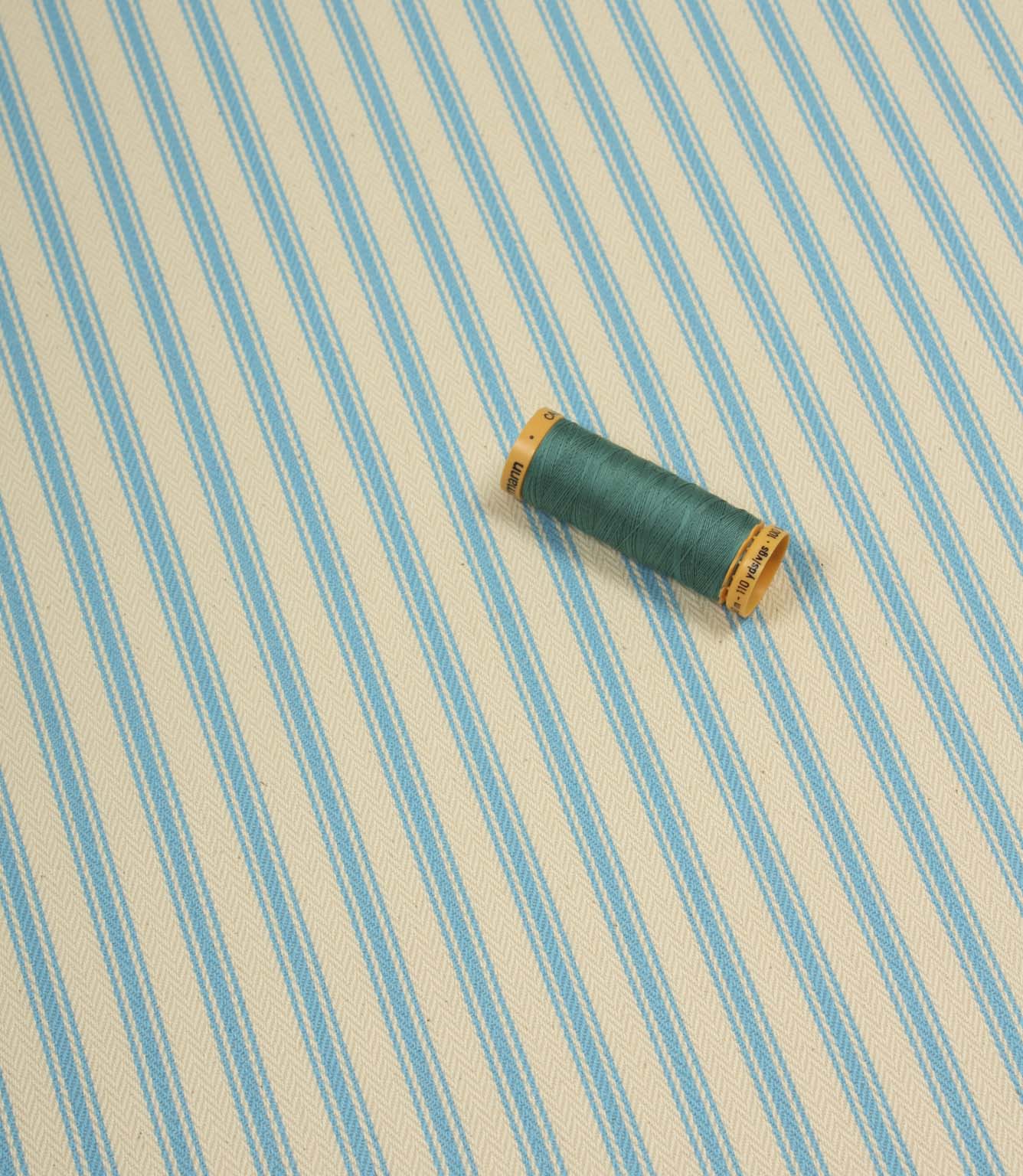 Pacific blue ticking stripe fabric shown on the diagonal with matching blue thread spool for colour reference.