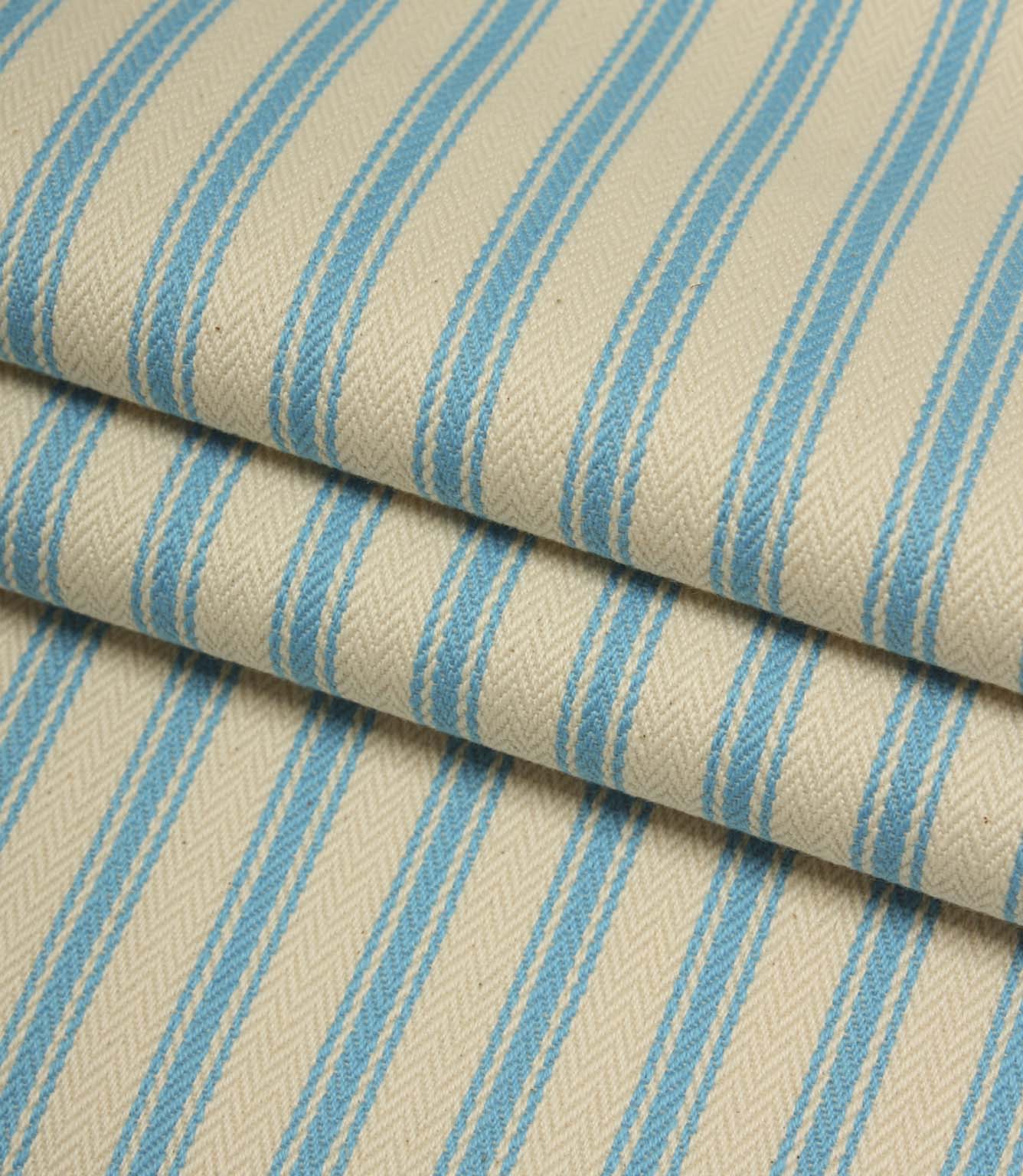 Folded ivory and Pacific blue striped ticking fabric highlighting the woven herringbone texture and soft drape.
