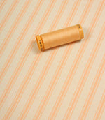 Peach ticking stripe fabric displayed on the diagonal with matching peach thread spool for colour reference.