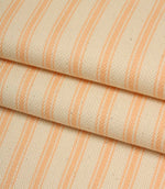 Folded ivory and peach striped ticking fabric showcasing the woven herringbone texture and soft natural finish.