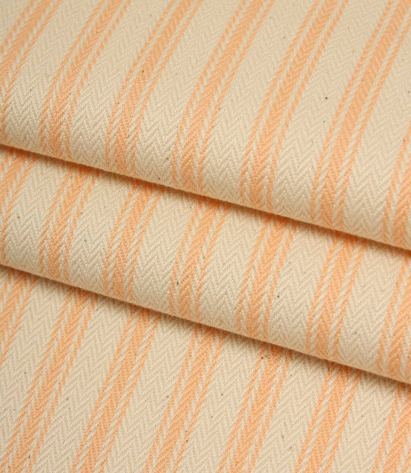 Folded ivory and peach striped ticking fabric showcasing the woven herringbone texture and soft natural finish.