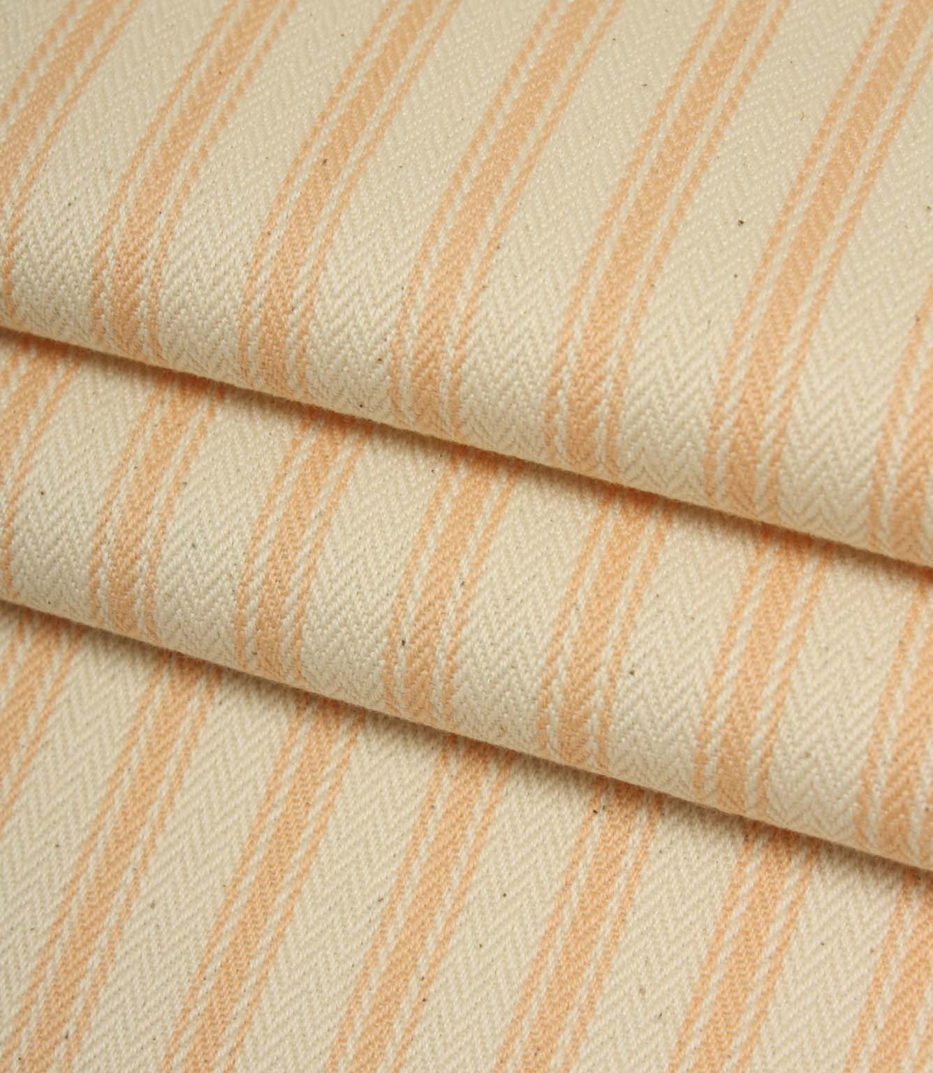 Folded ivory and peach striped ticking fabric showcasing the woven herringbone texture and soft natural finish.