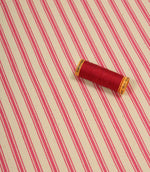 Petunia pink ticking stripe fabric displayed on the diagonal with matching pink thread spool for colour reference.