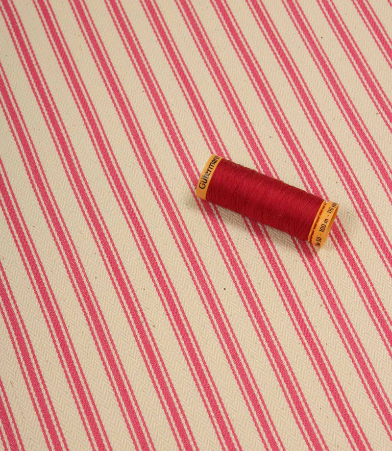 Petunia pink ticking stripe fabric displayed on the diagonal with matching pink thread spool for colour reference.