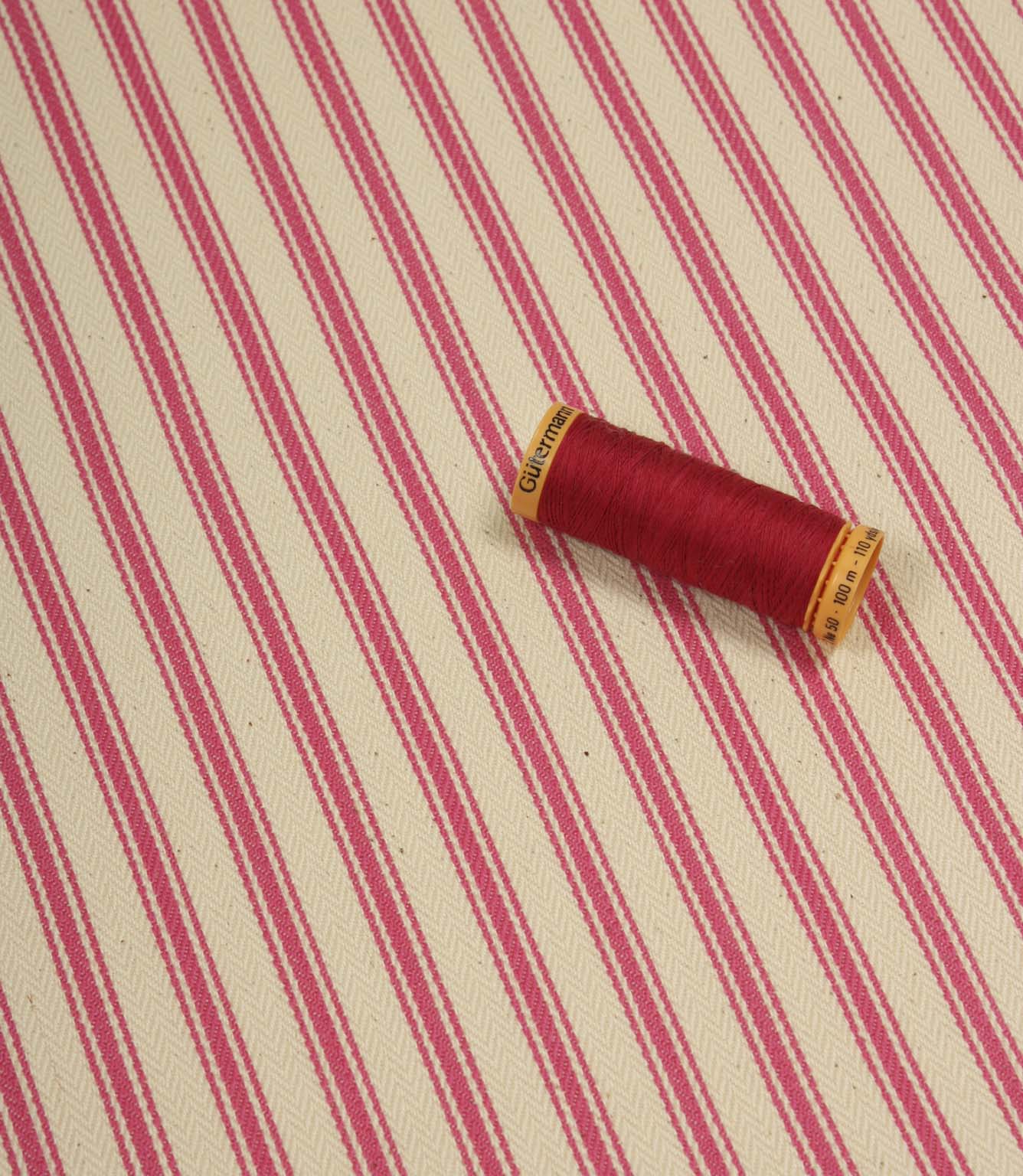 Petunia pink ticking stripe fabric displayed on the diagonal with matching pink thread spool for colour reference.