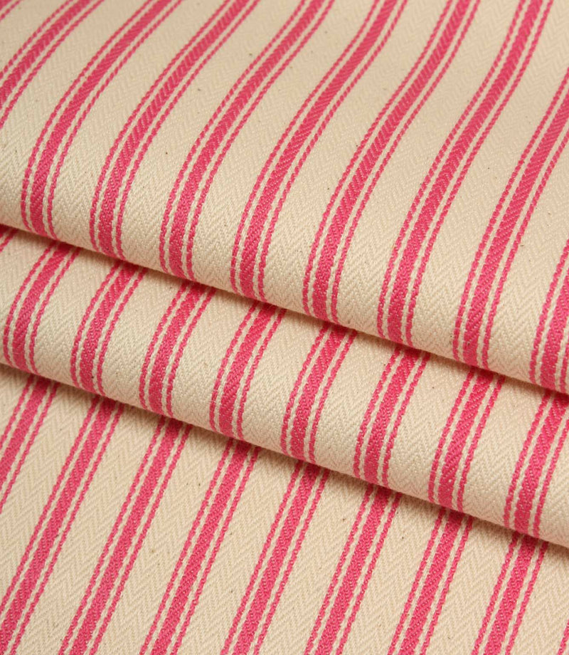 Folded ivory and petunia pink striped ticking fabric showcasing the woven herringbone texture and soft finish.