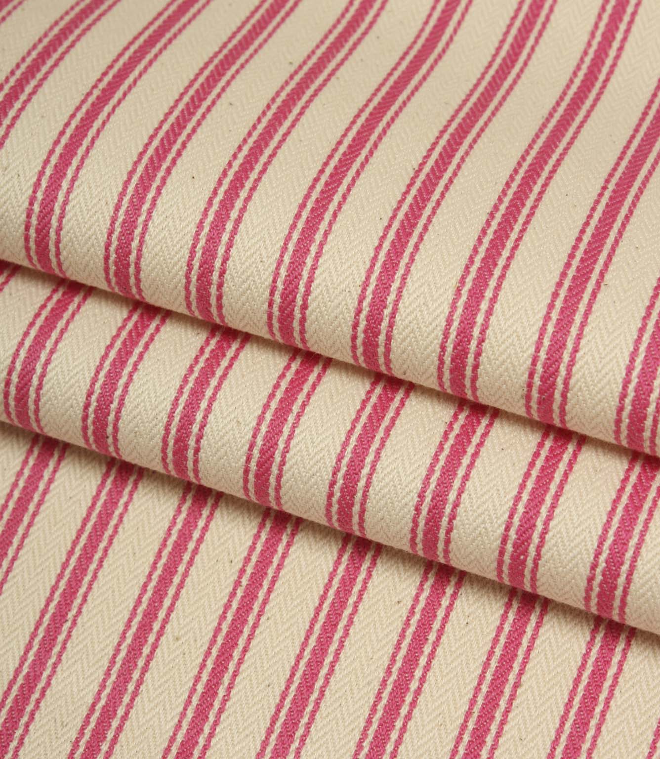 Folded ivory and petunia pink striped ticking fabric showcasing the woven herringbone texture and soft finish.