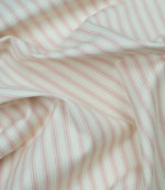 Pink ticking stripe fabric draped to show its soft handle, elegant stripe pattern and woven herringbone texture.