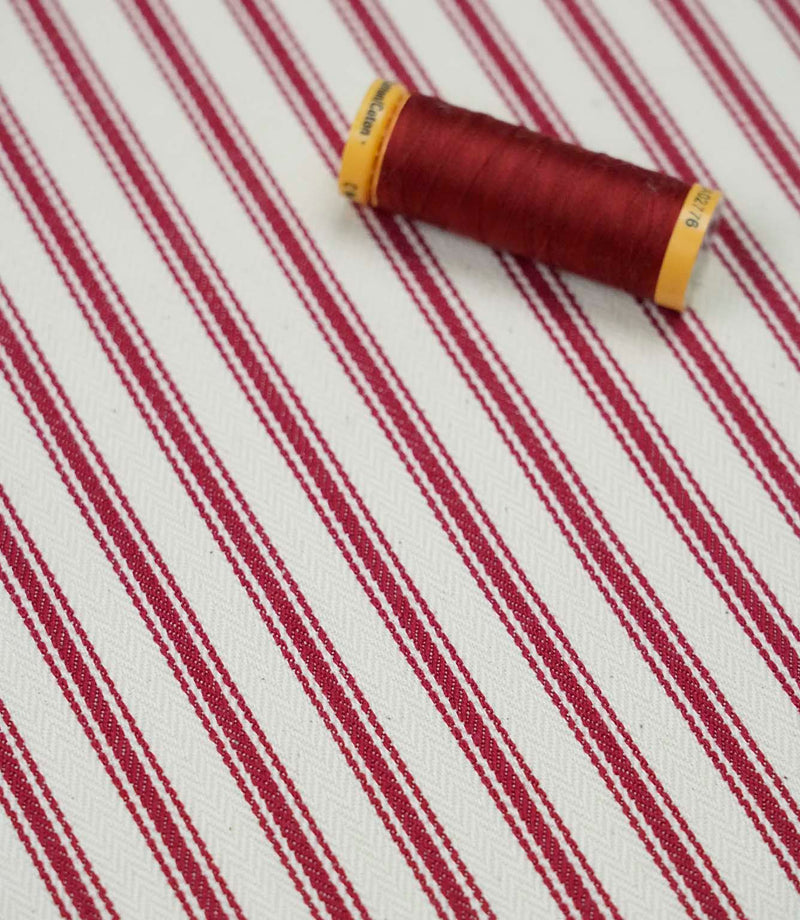 Red ticking stripe fabric with matching red thread, ideal for upholstery, curtains, blinds and sewing projects.