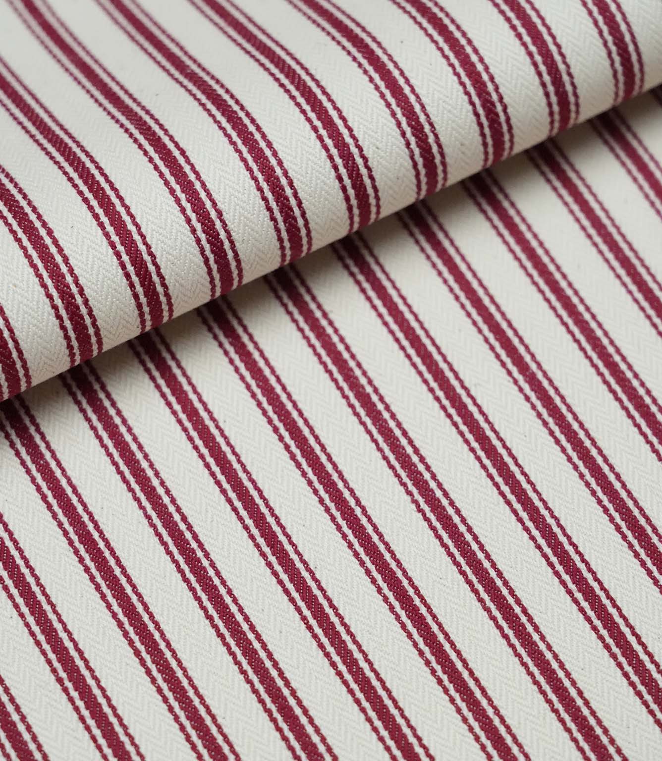 Folded red ticking stripe fabric showcasing the timeless striped pattern and premium woven herringbone finish.