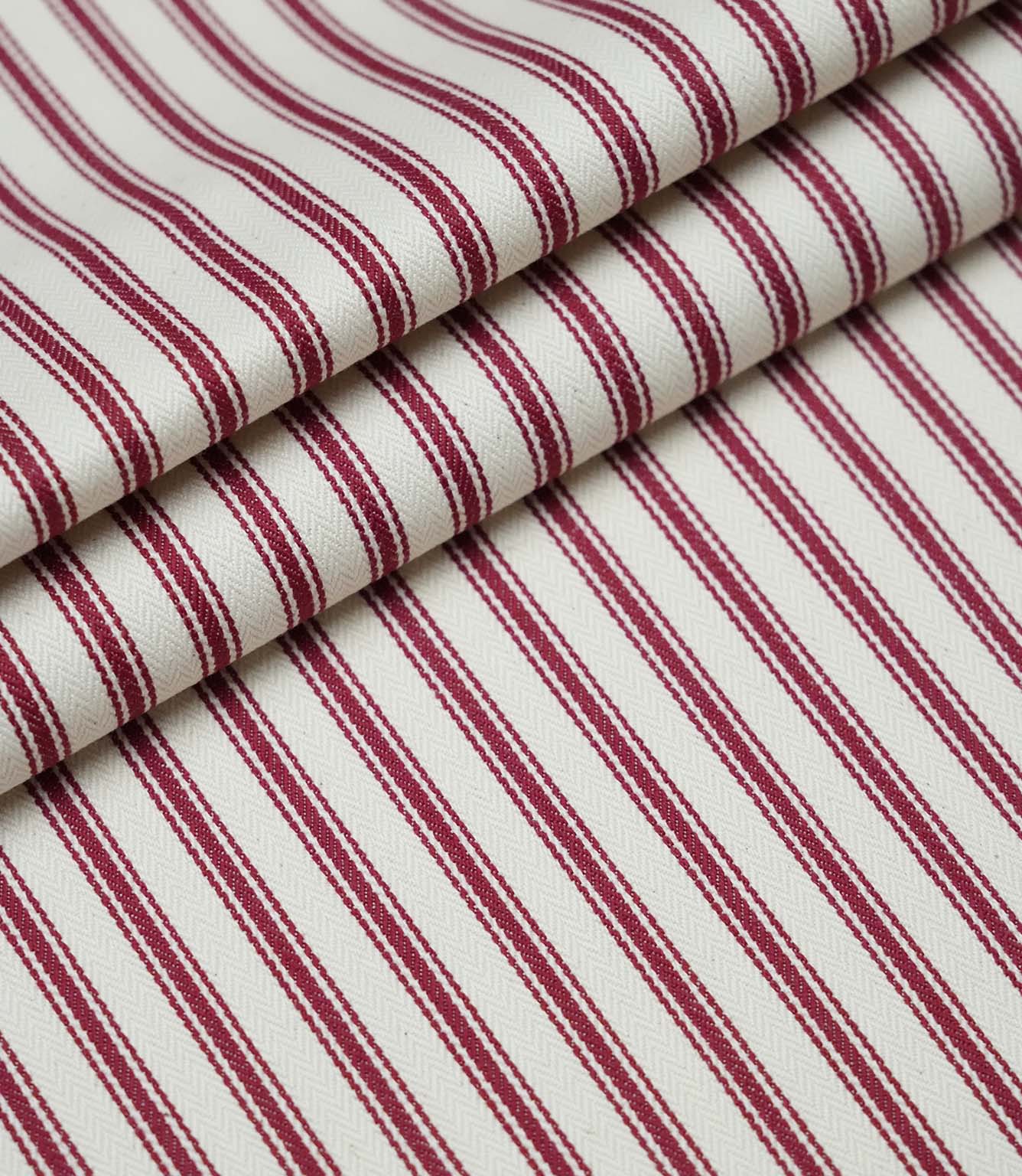 Layered folds of red ticking stripe fabric displaying the fine herringbone weave and classic striped design.