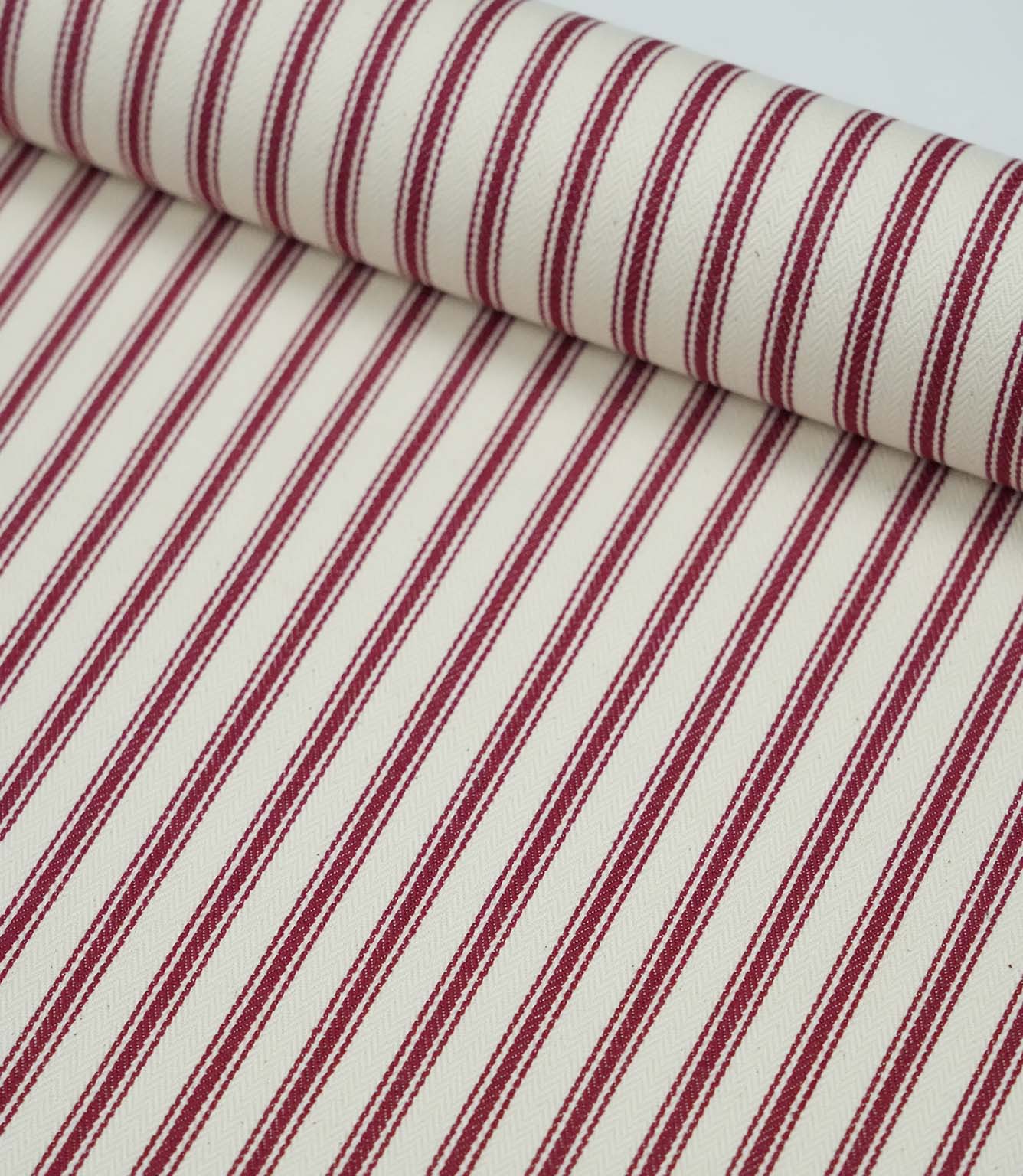 Rolled red ticking stripe fabric highlighting the classic striped design and subtle woven herringbone texture.