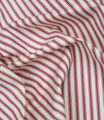 Red ticking stripe fabric draped to show its soft handle, elegant stripe pattern and woven herringbone texture.