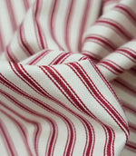 Close-up detail of red ticking stripe fabric showing the fine woven texture and bold red stripe pattern.