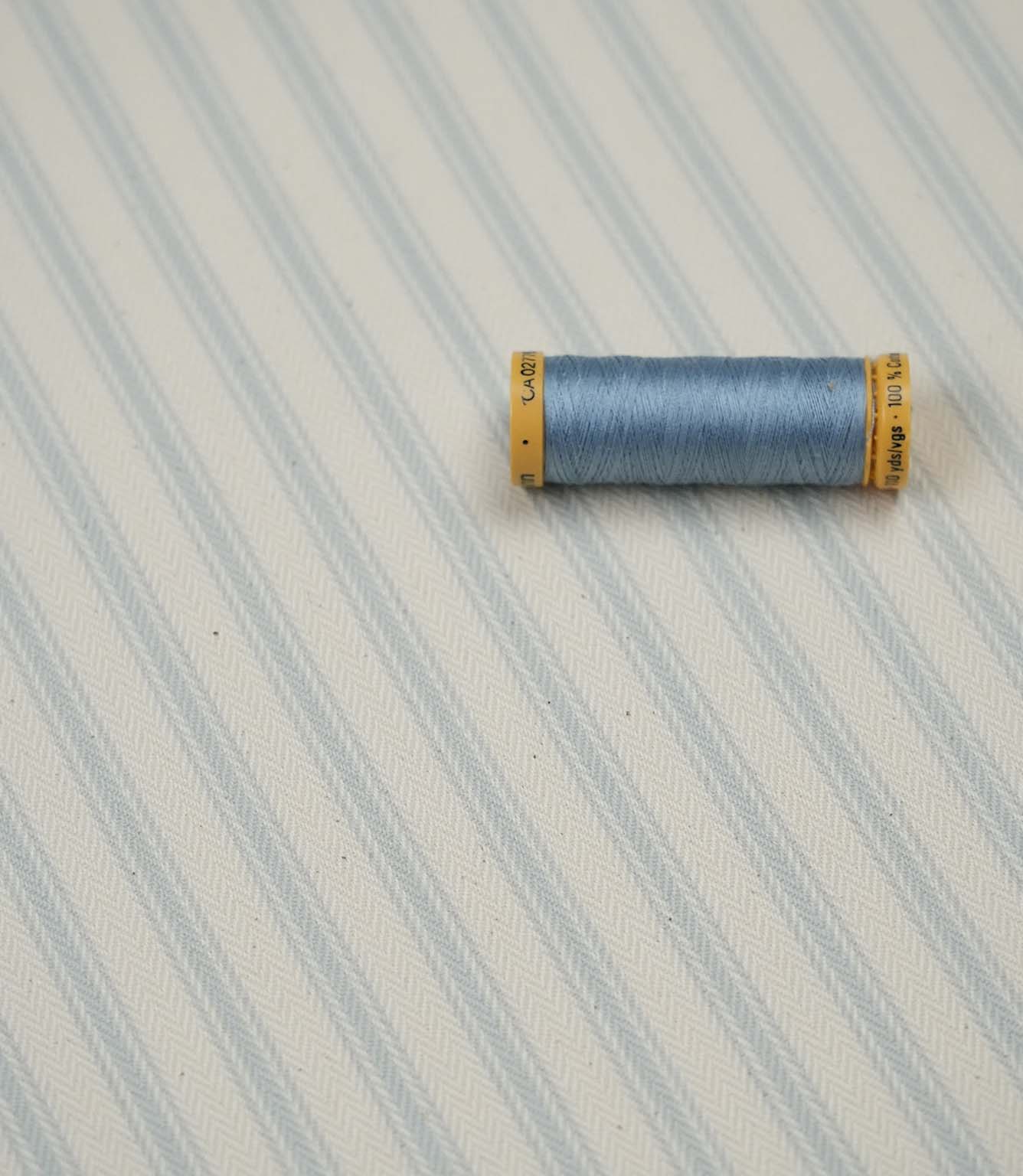 Sea Spray ticking stripe fabric with matching light blue thread, ideal for sewing, upholstery and home décor projects.