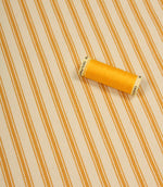 Turmeric yellow ticking stripe fabric shown on the diagonal with matching yellow thread spool for colour reference.