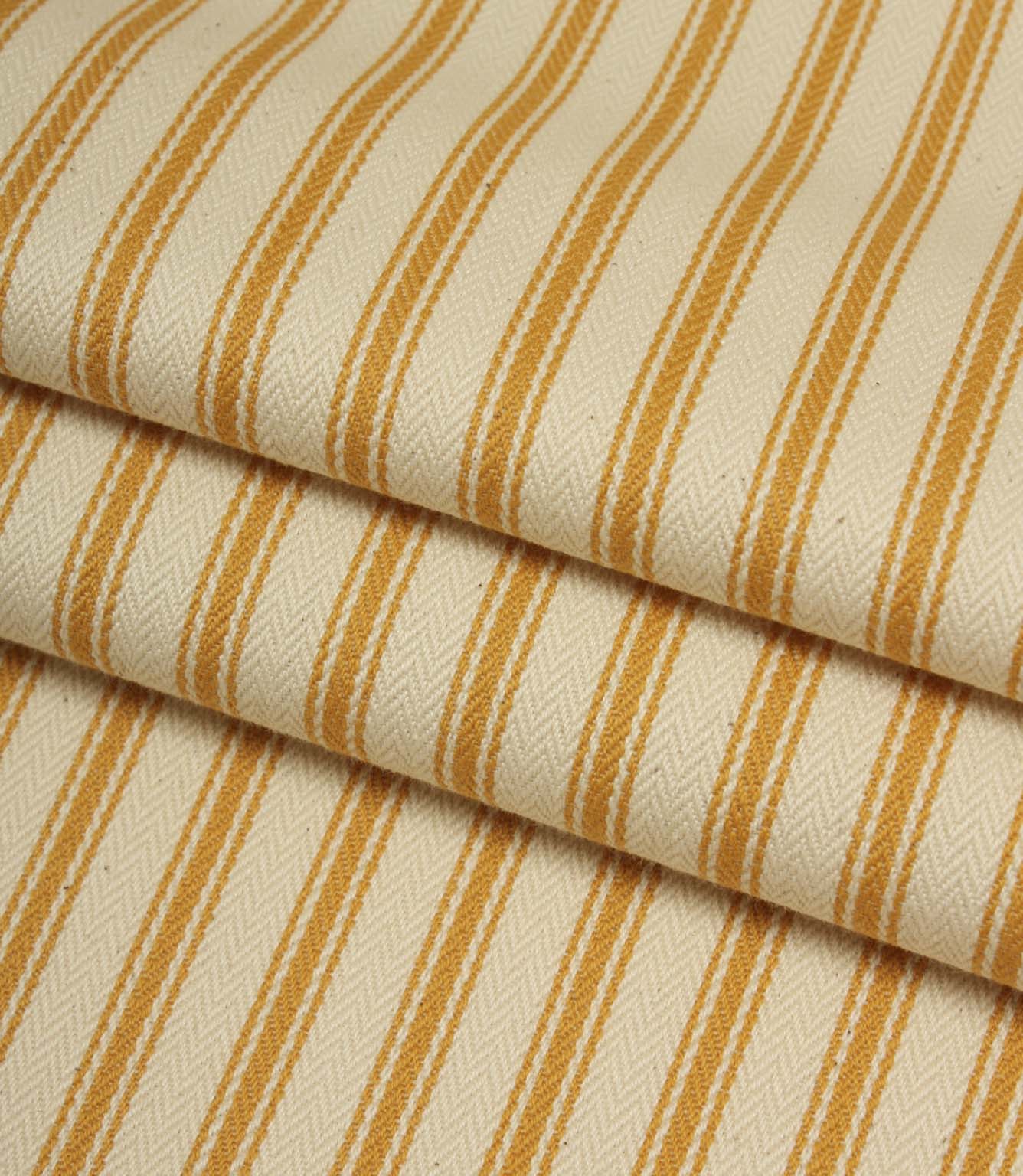 Folded ivory and turmeric yellow striped ticking fabric highlighting the woven herringbone texture and soft drape.