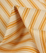 Detailed close-up of turmeric yellow striped ticking fabric with visible herringbone weave and soft textured folds.