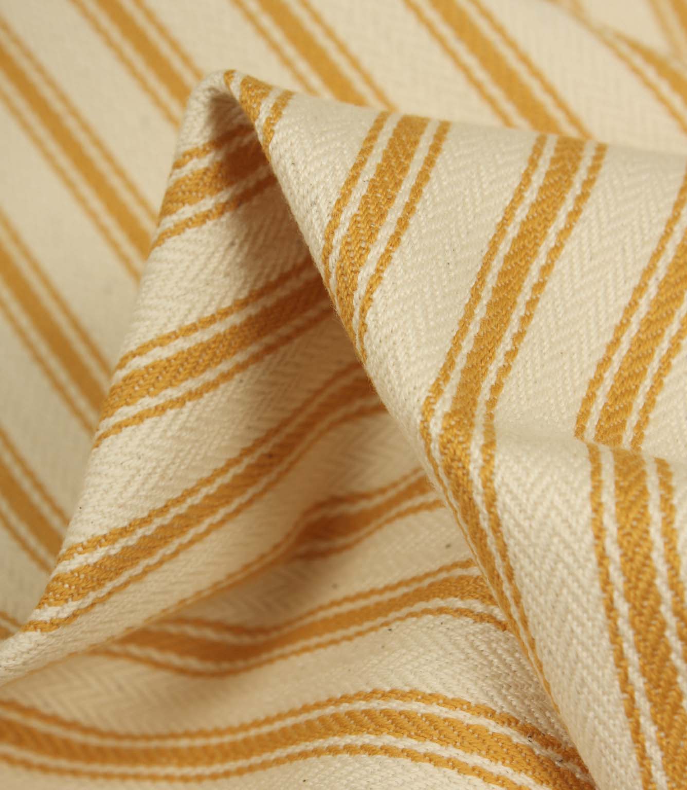 Detailed close-up of turmeric yellow striped ticking fabric with visible herringbone weave and soft textured folds.