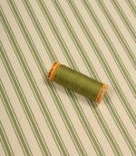 Warm green ticking stripe fabric displayed on the diagonal with matching green thread spool for colour reference.