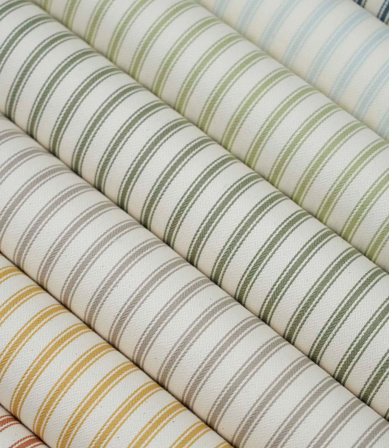 Collection of ticking stripe fabrics in sage green, duck egg blue, taupe, mustard and terracotta colourways, each featuring a classic striped design on an ivory herringbone weave.