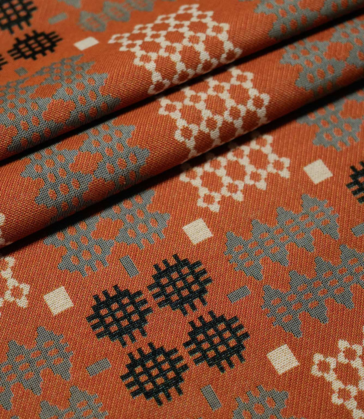 Kinfolk fabric arranged in neat folds, showing the scale and repetition of the geometric pattern in terracotta orange, grey, black and cream.