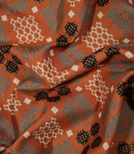 Kinfolk fabric loosely draped to show how the material falls, with geometric woven-style motifs in grey, black and cream on a terracotta orange background.
