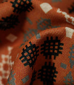 Macro close-up of folded Kinfolk fabric, showing the textured weave and black geometric motif against the terracotta orange ground.