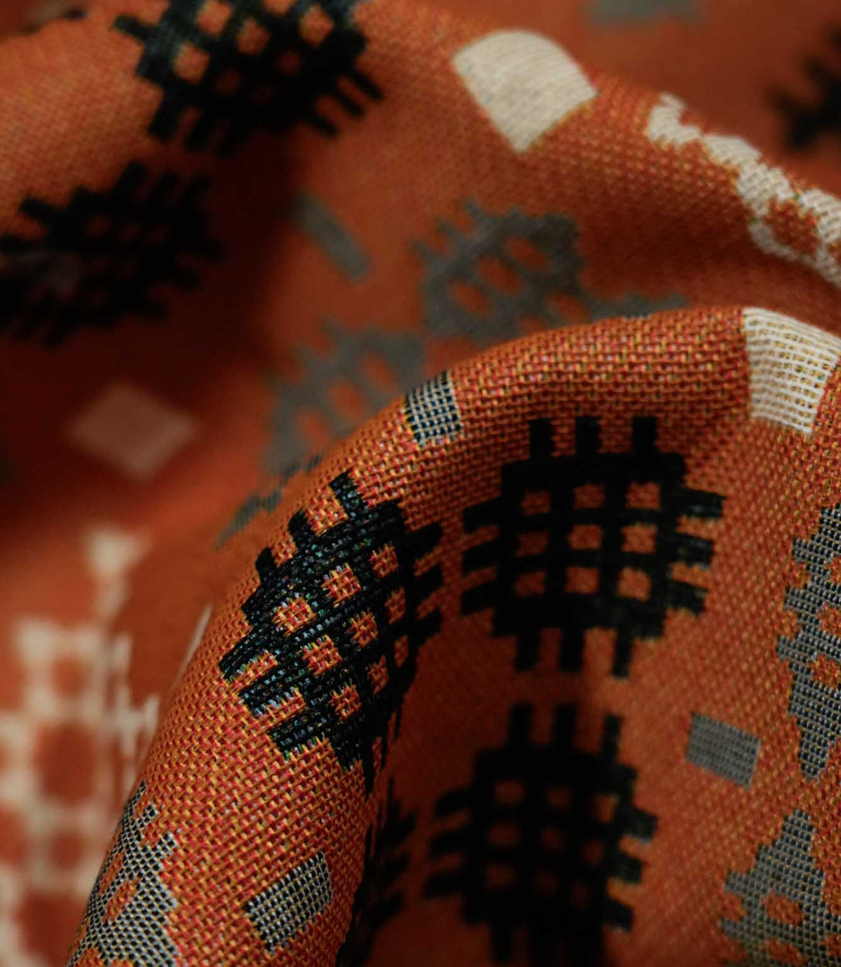 Macro close-up of folded Kinfolk fabric, showing the textured weave and black geometric motif against the terracotta orange ground.