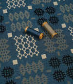 Kinfolk geometric fabric in terracotta orange with coordinating thread spools highlighting its grey and orange tones.