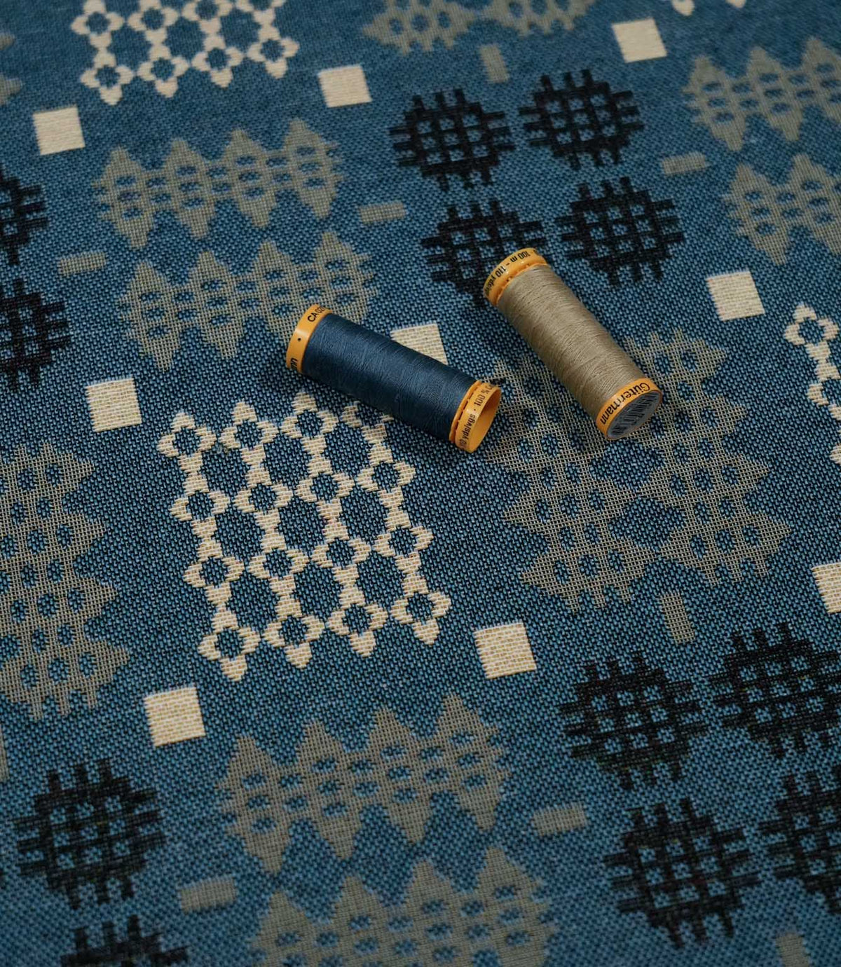 Kinfolk geometric fabric in terracotta orange with coordinating thread spools highlighting its grey and orange tones.
