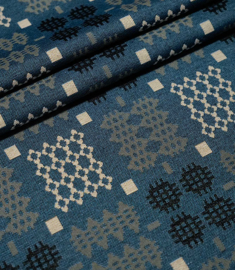 Kinfolk fabric arranged in soft folds, showing its terracotta orange ground and repeating geometric pattern.